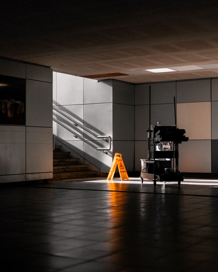 A well-lit underground corridor featuring stairs, cleaning supplies, and warning signs.